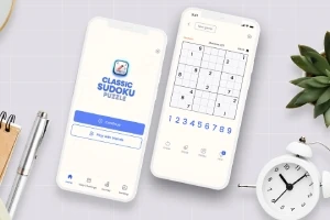 Hai điện thoại hiển thị ứng dụng trò chơi đố số trên bàn với đồng hồ trắng, sổ ghi chép, bút và cây xanh