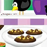 Một con chim đứng trên bậu cửa sổ gần đĩa bánh quy sô cô la và hạt điều trong nhà bếp có dụng cụ bào và thanh sô cô la