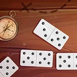 Các quân cờ domino màu trắng nằm trên bề mặt gỗ nâu, bên cạnh một chiếc la bàn cổ điển
