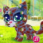 Một chú mèo con có mắt to, lông cắm hoa hồng nhỏ đứng trên nền cỏ xanh với một bàn tay chỉ vào các đồ vật ở góc trái