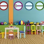 Phòng trẻ em với bàn ghế nhỏ, bảng và đồ chơi nhiều màu sắc trên nền tường gắn các cửa sổ tròn