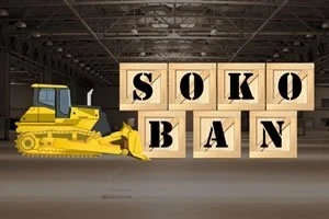 Một máy ủi màu vàng đứng trong nhà kho phía trước các khối gỗ xếp thành chữ SOKOBAN