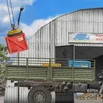 Một chiếc xe tải đang đậu trước nhà kho với cần cẩu đang nâng một thùng hàng màu đỏ