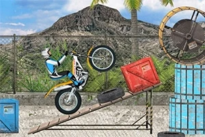 Một chiếc xe máy địa hình đang thực hiện động tác nhảy trên dốc, xung quanh là các thùng gỗ, bánh xe và núi non phía sau