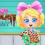 Cô bé tóc vàng với nơ hồng lớn cầm hộp sô cô la cạnh dòng chữ Yummy Chocolate Factory trên nền xanh